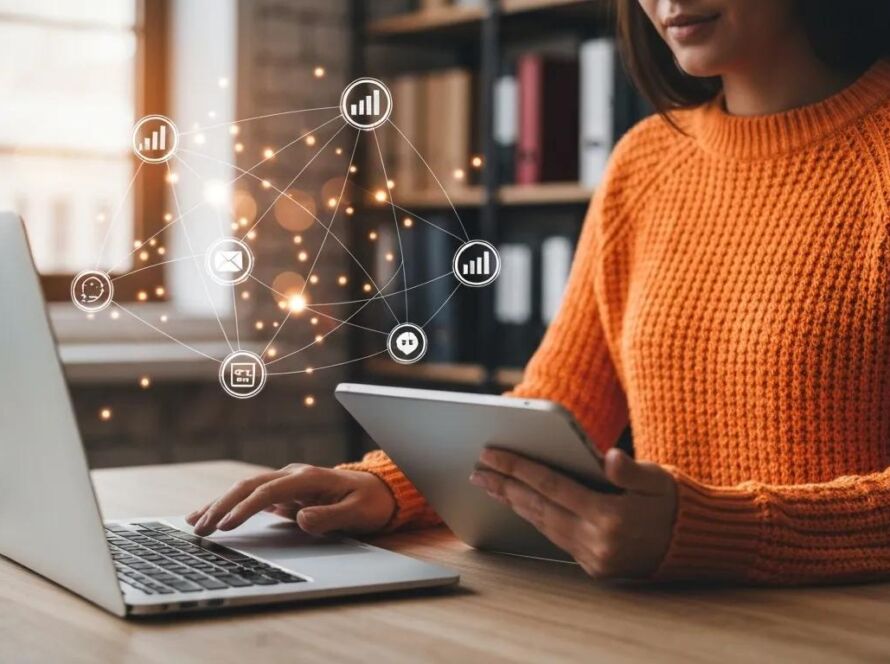 Kvinna i orange tröja arbetar vid laptop och surfplatta med digitala ikoner som symboliserar data, e-post och nätverk – ett visuellt koncept för Marketing as a Service (MaaS).